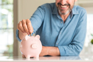 man putting coins into a pink piggy bank