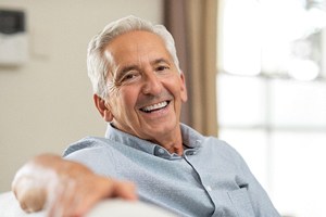 IHappy senior man reclining on couch, enjoying his implant dentures