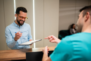 a front desk staff member handing a patient forms to fill out