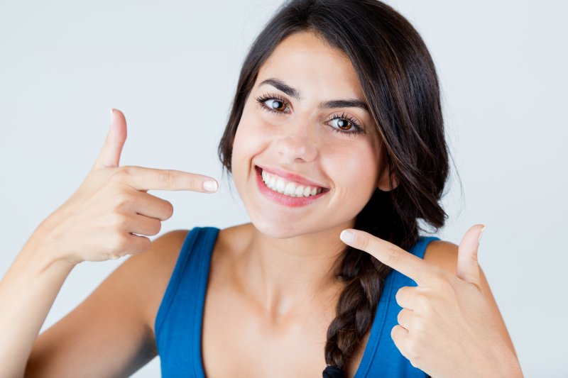 young woman smiling and pointing at white teeth