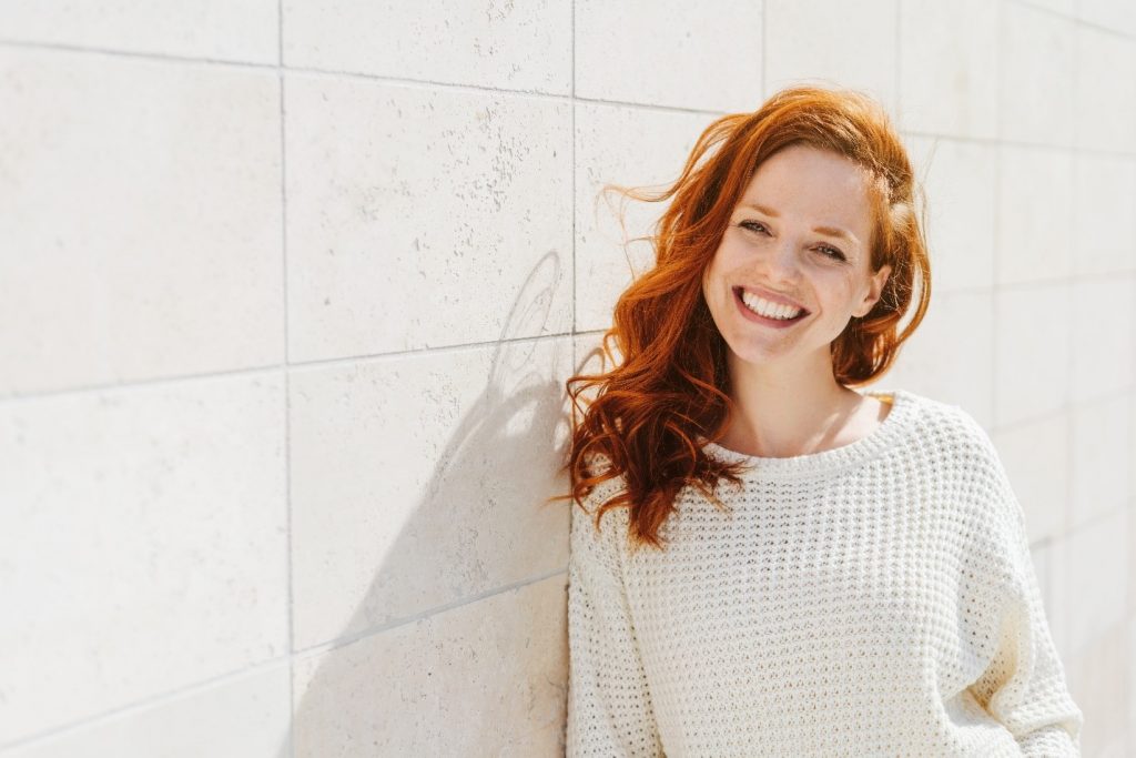 Woman with red hair and white teeth smiling outside